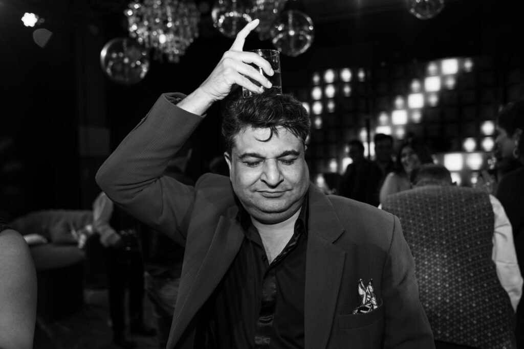 A man in a suit is balancing a shot glass on his head in a black and white photo.