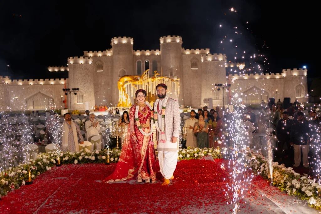Bride and groom walking down a rose-petal aisle with fireworks and a lit-up fort backdrop at their wedding entrance