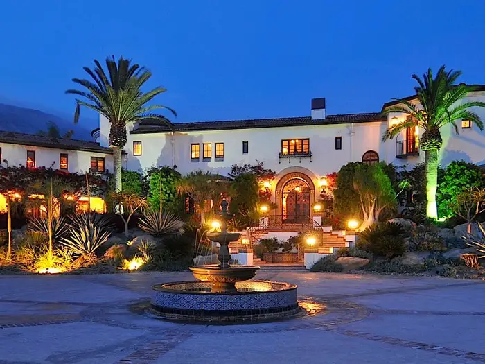 Hummingbird Nest Ranch at dusk, a white Spanish-style villa with a red-tiled roof, glowing lanterns.