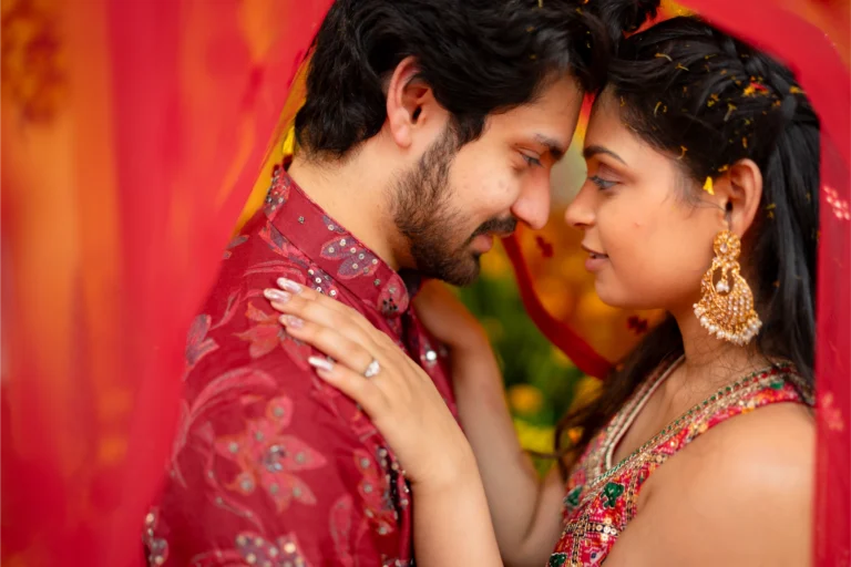 Couple forehead to forehead against a red and orange backdrop.