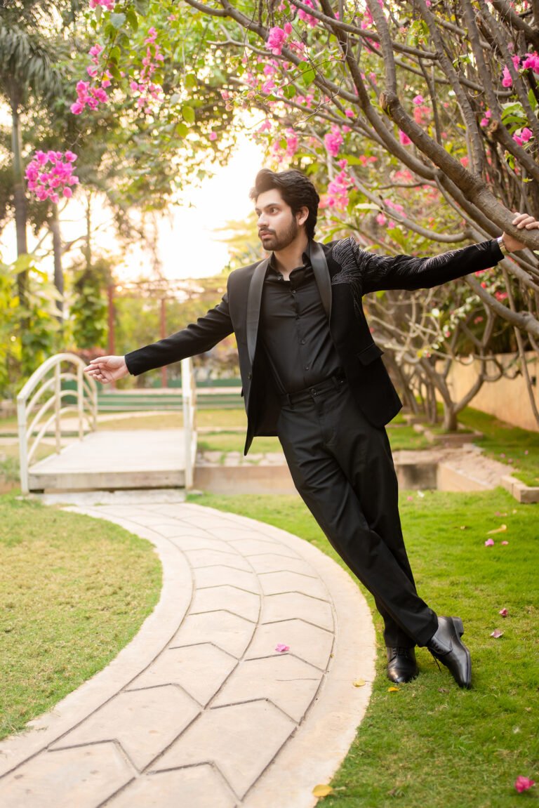 Lohith in a black suit leaning back with arms outstretched in a garden.