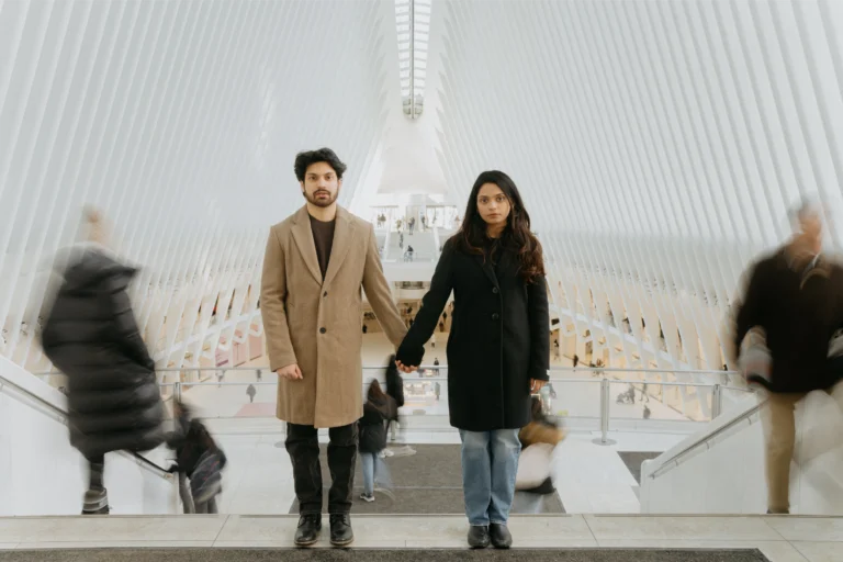 Couple in winter coats standing in a bright white station hall.