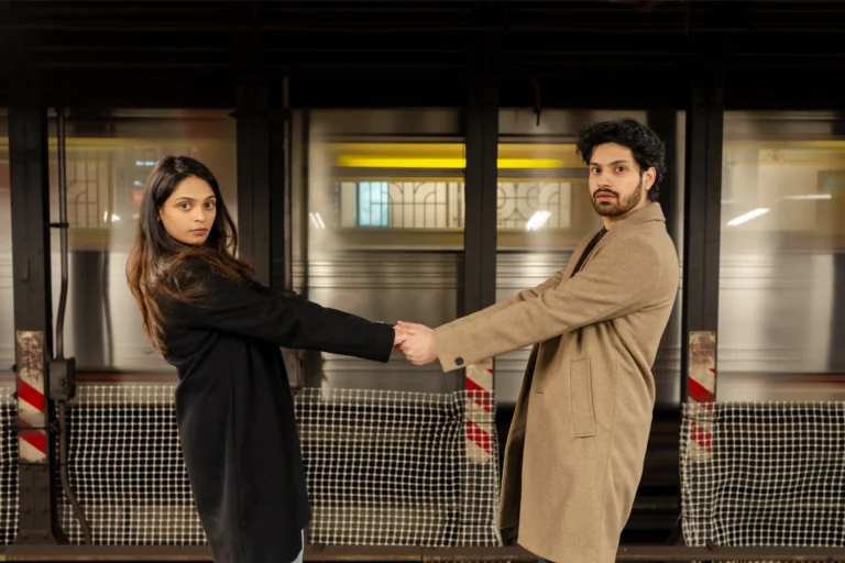 Srija & Lohith holding hands at arm's length on a subway platform.