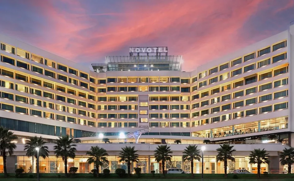 Novotel Visakhapatnam hotel at dusk, a curved white building with lit windows.