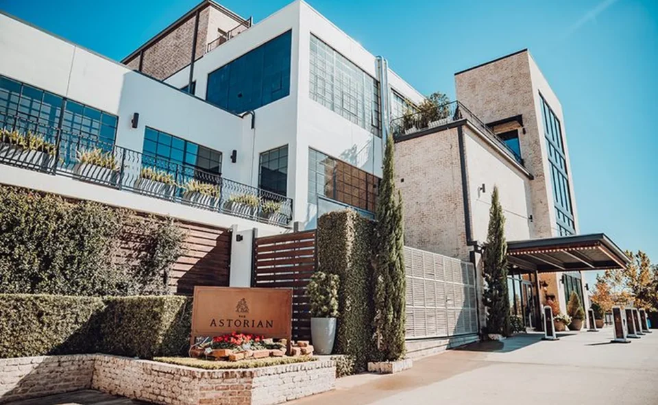 The Astorian hotel entrance with a brick planter sign, tall cypress trees.