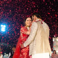 Bride and groom embracing under a shower of red petals.