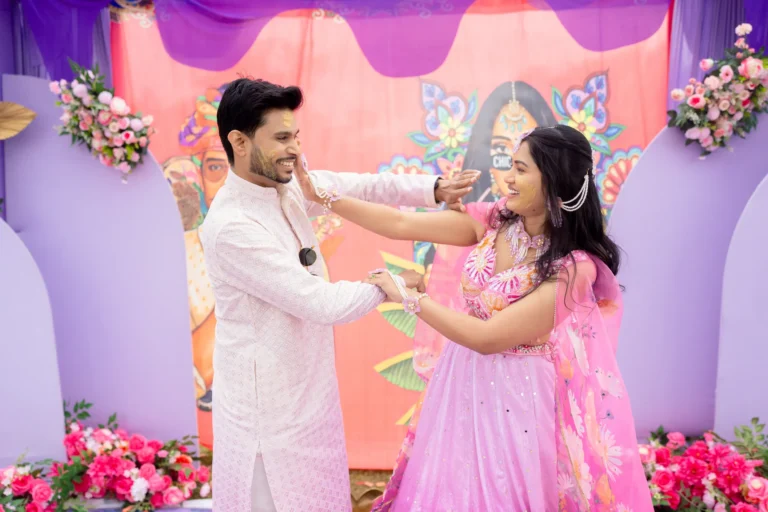Bride reaching to put turmeric on the groom's face as he laughs.