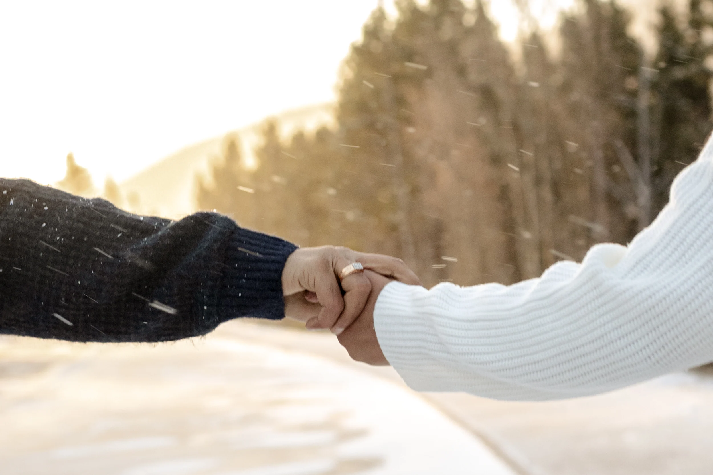 Hands held together in falling snow with the engagement ring visible.